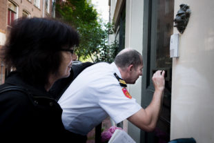 Een handhaver kijkt door een brievenbusgleuf of mensen in het pand aan de Schipperstraat aanwezig zijn.